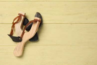 Photo of Slingshot with stones on yellow wooden background, top view. Space for text