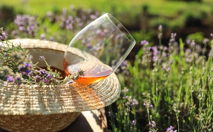 Photo of Straw hat and glass of wine on wooden table in lavender field