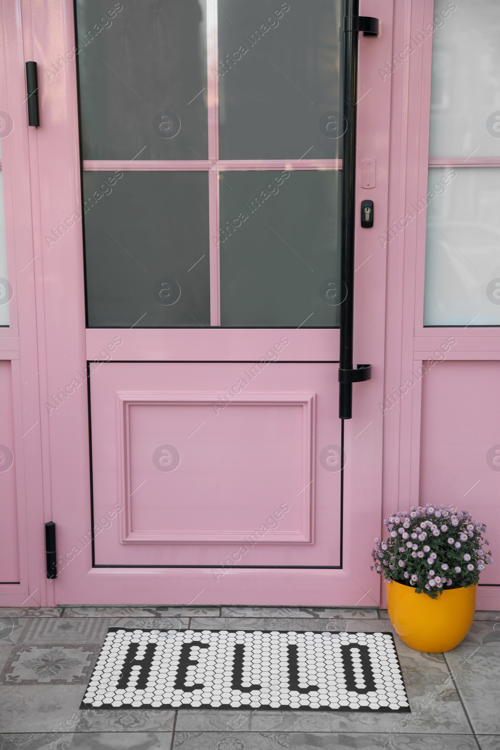 Photo of Stylish door mat with word HELLO and beautiful flowers near entrance