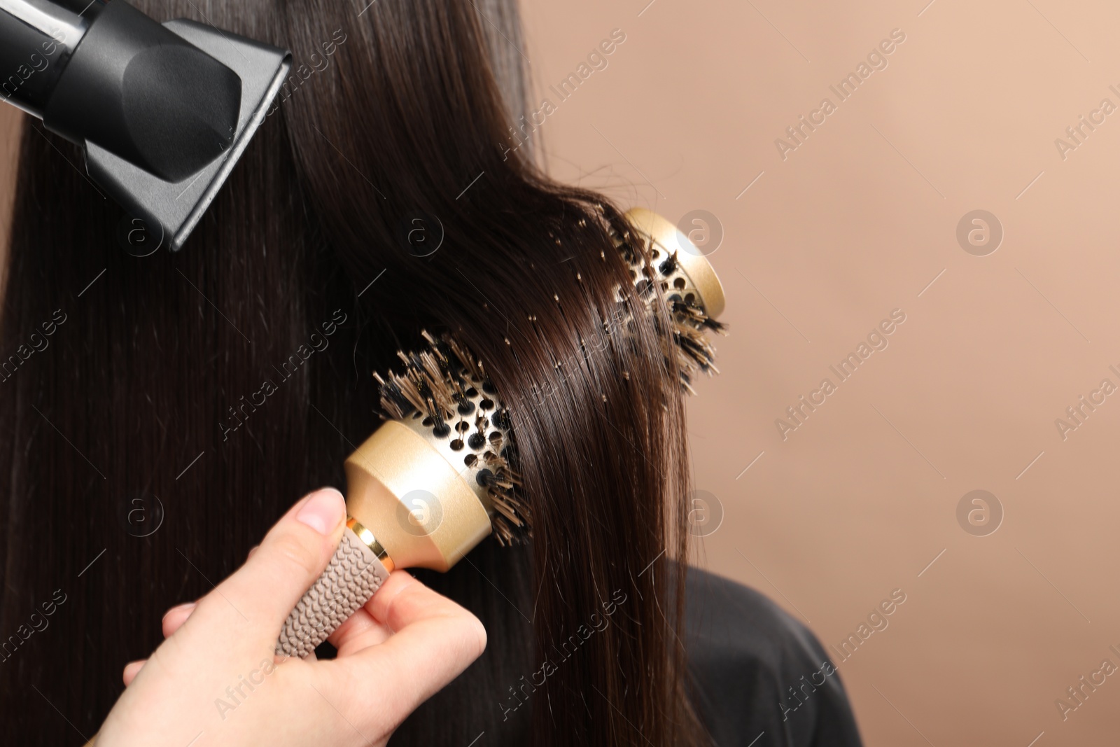 Photo of Hairdresser blow drying client's hair on beige background, closeup. Space for text