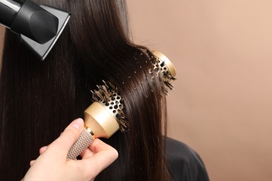 Photo of Hairdresser blow drying client's hair on beige background, closeup. Space for text