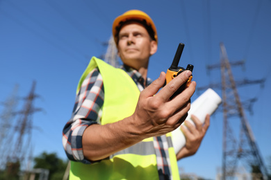 Photo of Professional electrician near high voltage tower, focus on hand with portable radio station