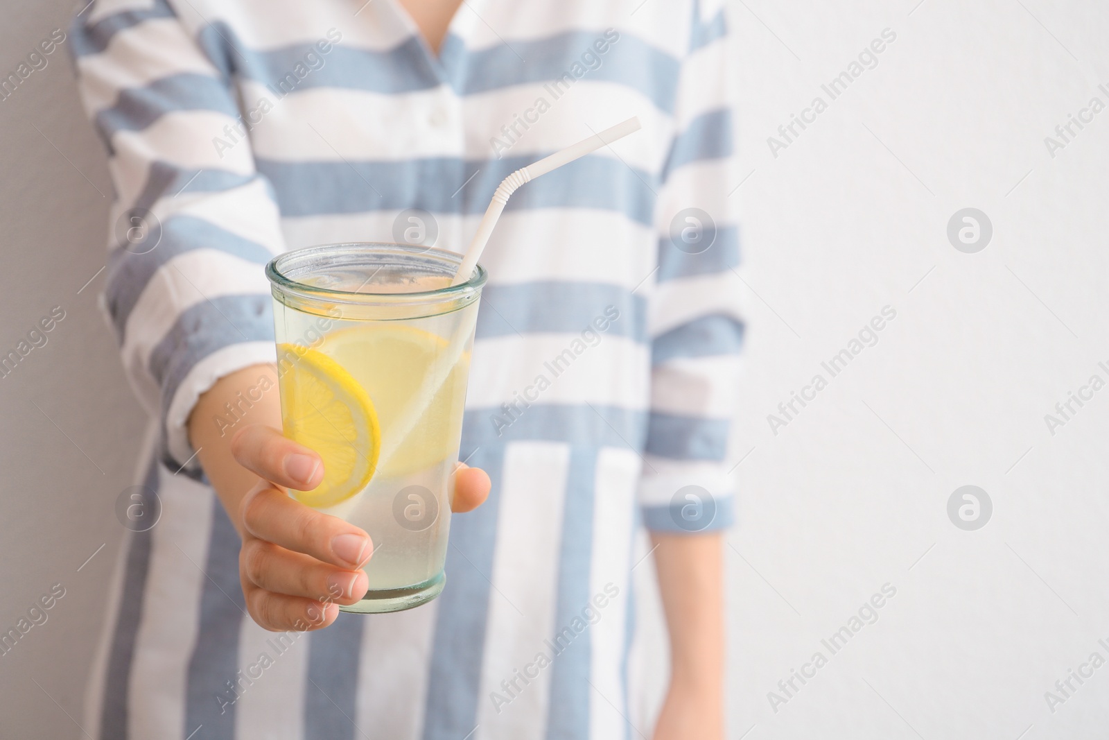 Photo of Young woman holding glass with lemon cocktail against light background