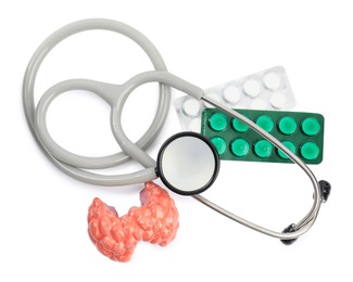 Photo of Plastic model of afflicted thyroid, pills and stethoscope on white background, top view