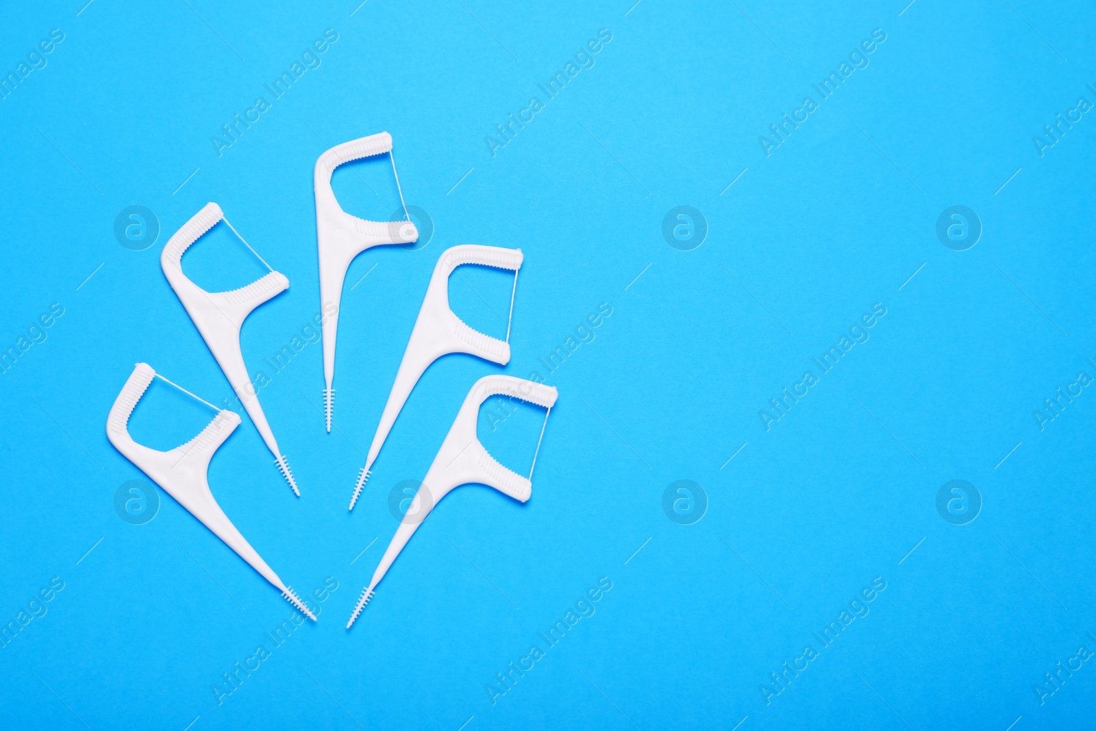 Photo of Dental flossers on light blue background, flat lay. Space for text