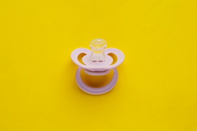 Photo of New baby pacifier on yellow background, top view