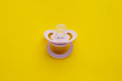 New baby pacifier on yellow background, top view