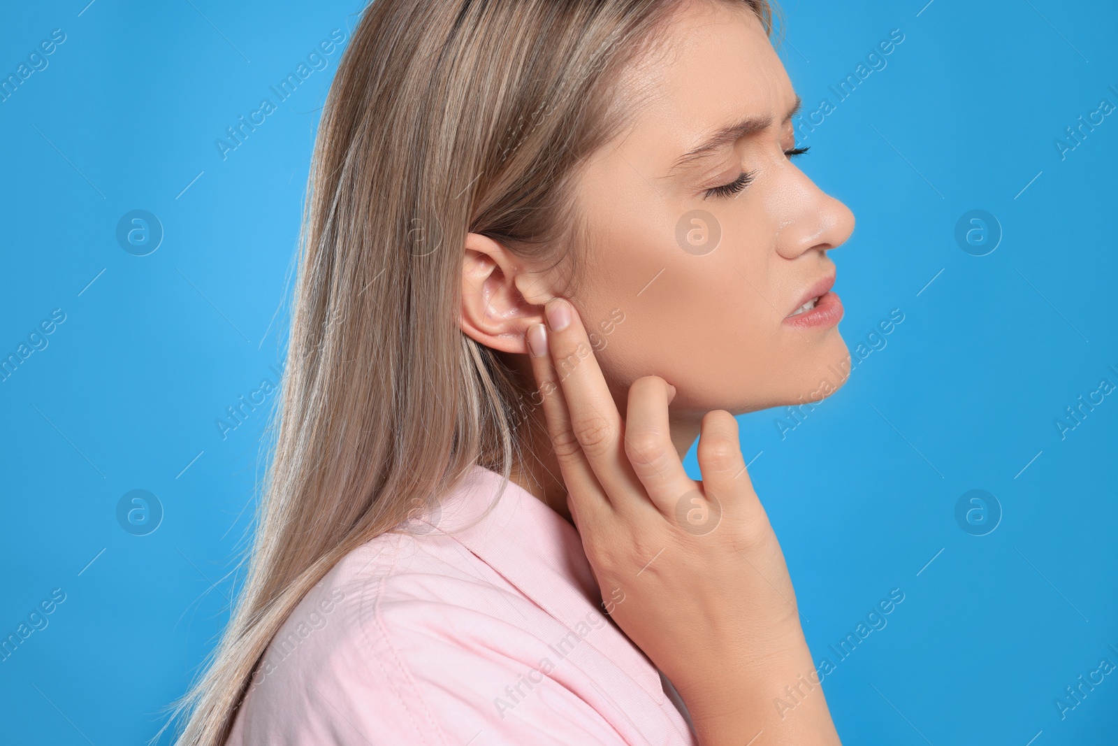 Photo of Young woman suffering from ear pain on light blue background