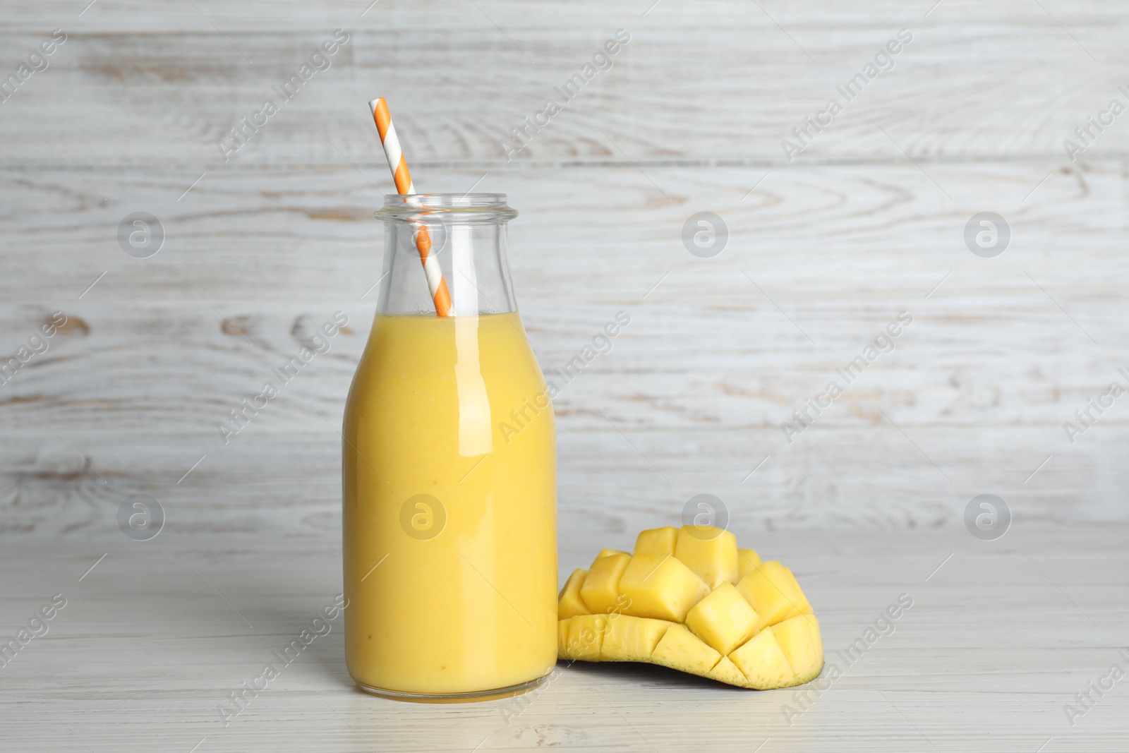 Photo of Bottle of tasty smoothie with straw and mango on white wooden table