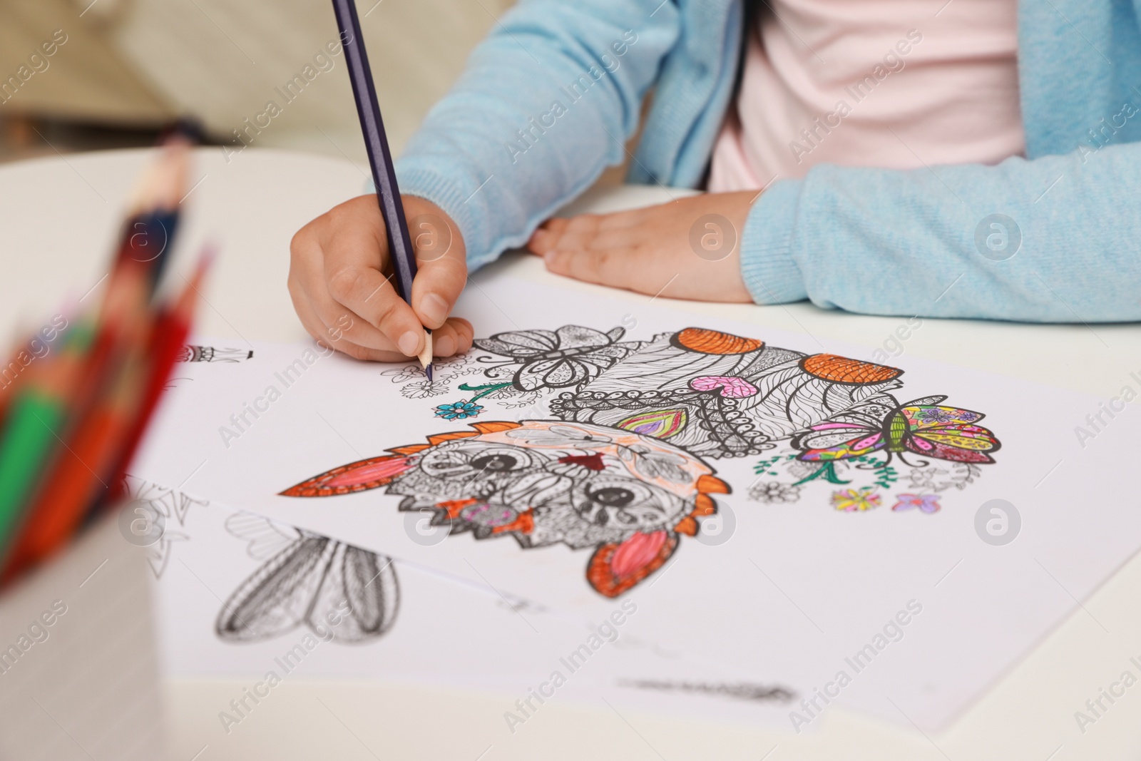 Photo of Little girl coloring antistress page at table, closeup