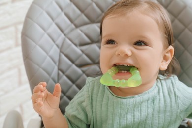 Photo of Cute little baby nibbling teether in high chair indoors, closeup