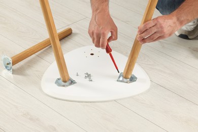 Photo of Man with screwdriver assembling furniture on floor, closeup