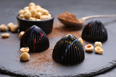 Photo of Tasty chocolate candies and nuts on slate plate, closeup