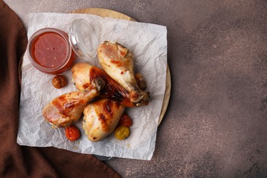 Marinade, roasted chicken drumsticks and tomatoes on brown table, top view. Space for text