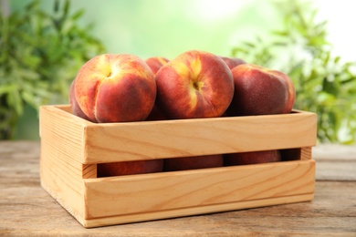 Wooden crate with tasty peaches on table against green blurred background