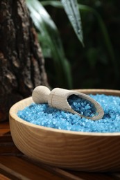 Photo of Bowl of blue sea salt with scoop on wooden table, closeup