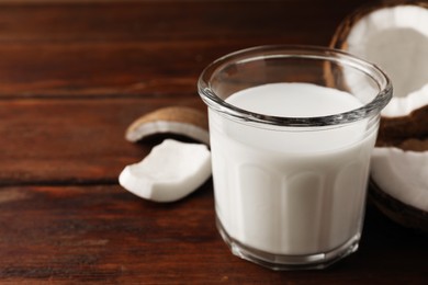 Glass of delicious vegan milk and coconut pieces on wooden table, space for text