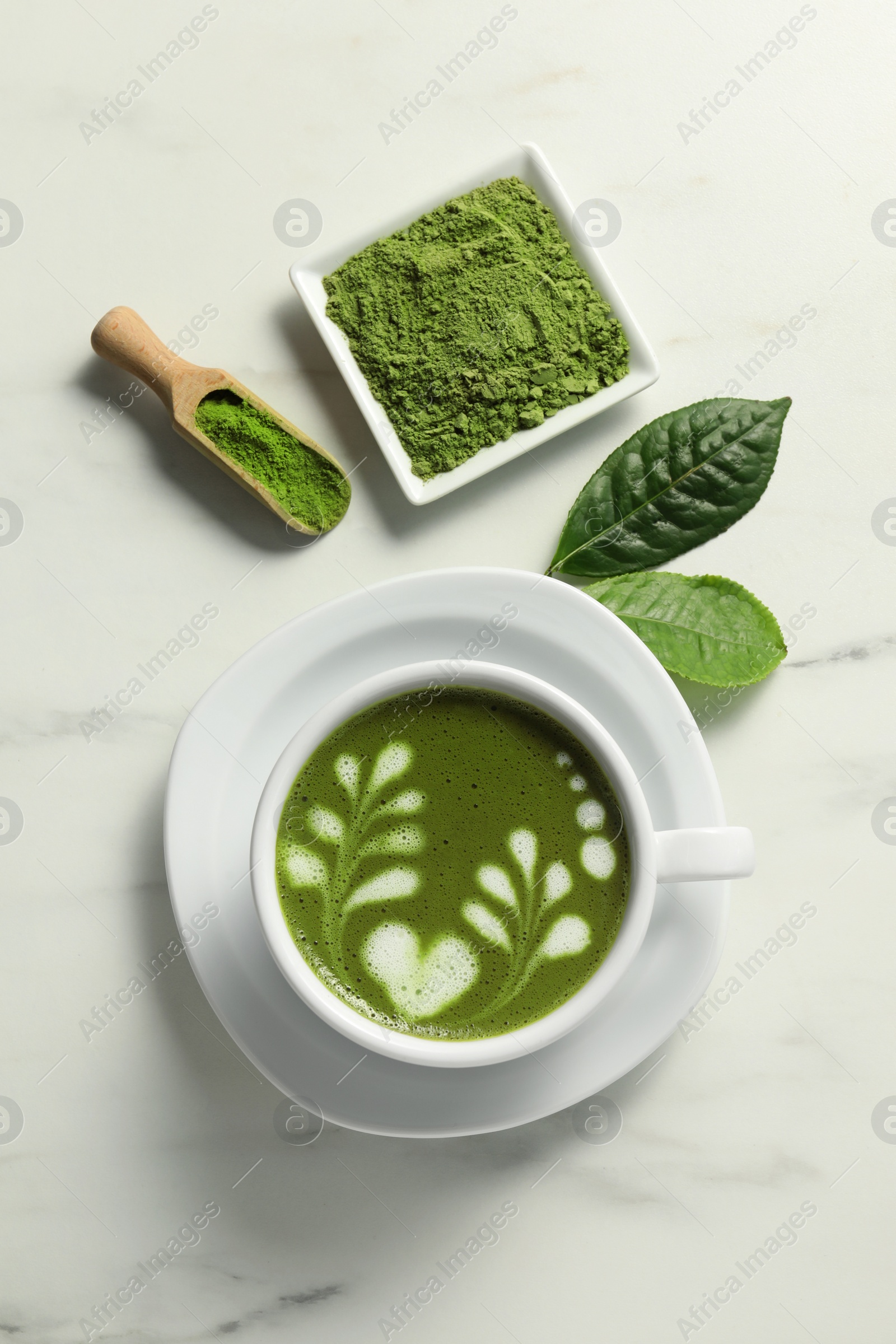 Photo of Delicious matcha latte, powder and leaves on white marble table, flat lay