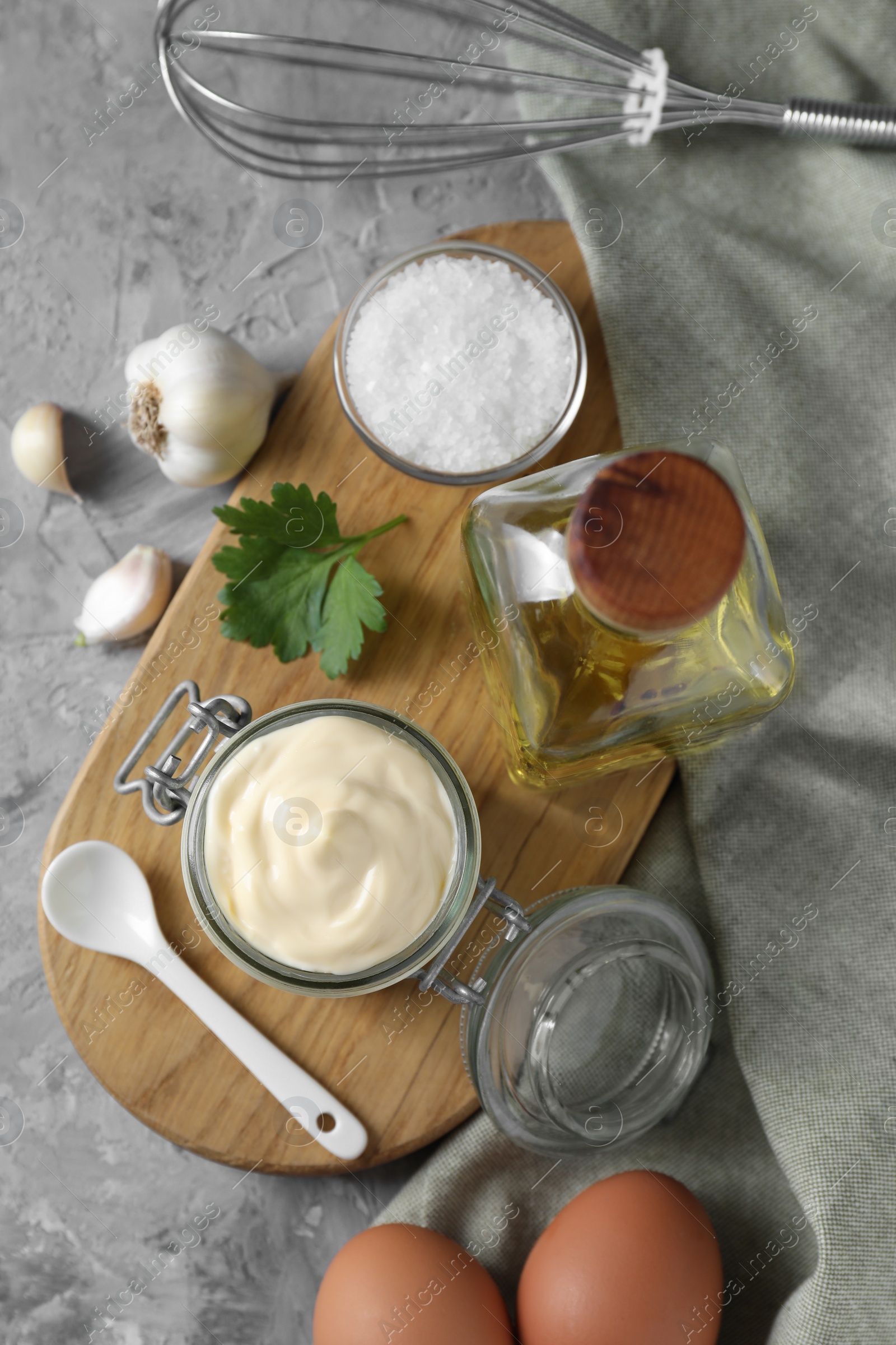 Photo of Tasty mayonnaise in jar, ingredients and whisk on gray table, flat lay