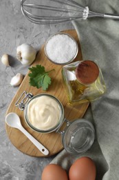 Tasty mayonnaise in jar, ingredients and whisk on gray table, flat lay