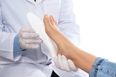 Male orthopedist fitting insole on patient's foot against white background, closeup