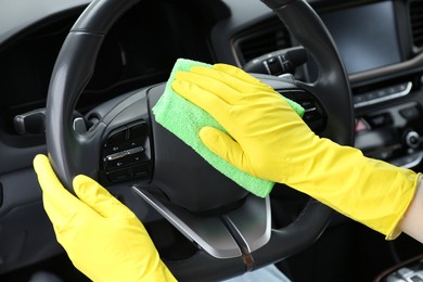 Photo of Woman cleaning steering wheel with rag in car, closeup