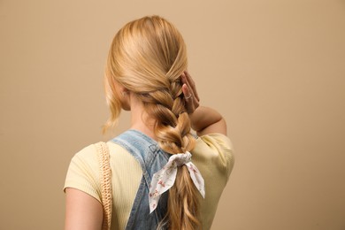 Young woman with stylish bandana on beige background, back view