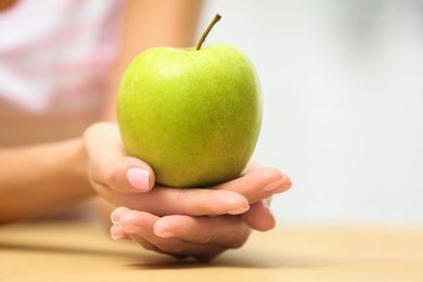 Photo of Woman holding fresh green apple at table, closeup. Space for text