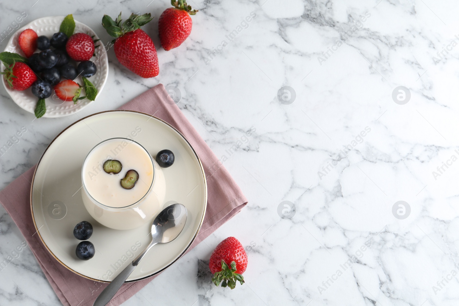 Photo of Tasty yogurt in glass and berries on white marble table, flat lay. Space for text