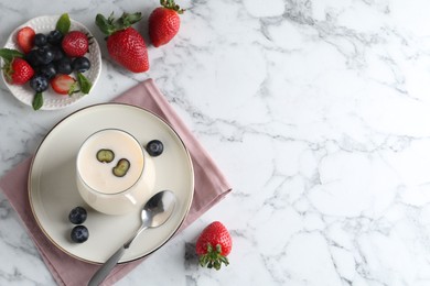 Photo of Tasty yogurt in glass and berries on white marble table, flat lay. Space for text