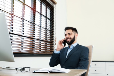 Photo of Handsome businessman talking on phone while working with computer at table in office