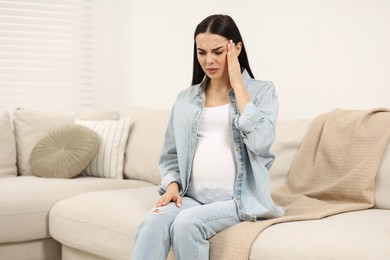 Photo of Pregnant woman suffering from headache on sofa at home