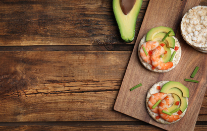 Puffed rice cakes with shrimps and avocado on wooden table, flat lay. Space for text