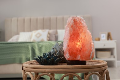 Beautiful Himalayan salt lamp and lotus figures on wicker table in bedroom