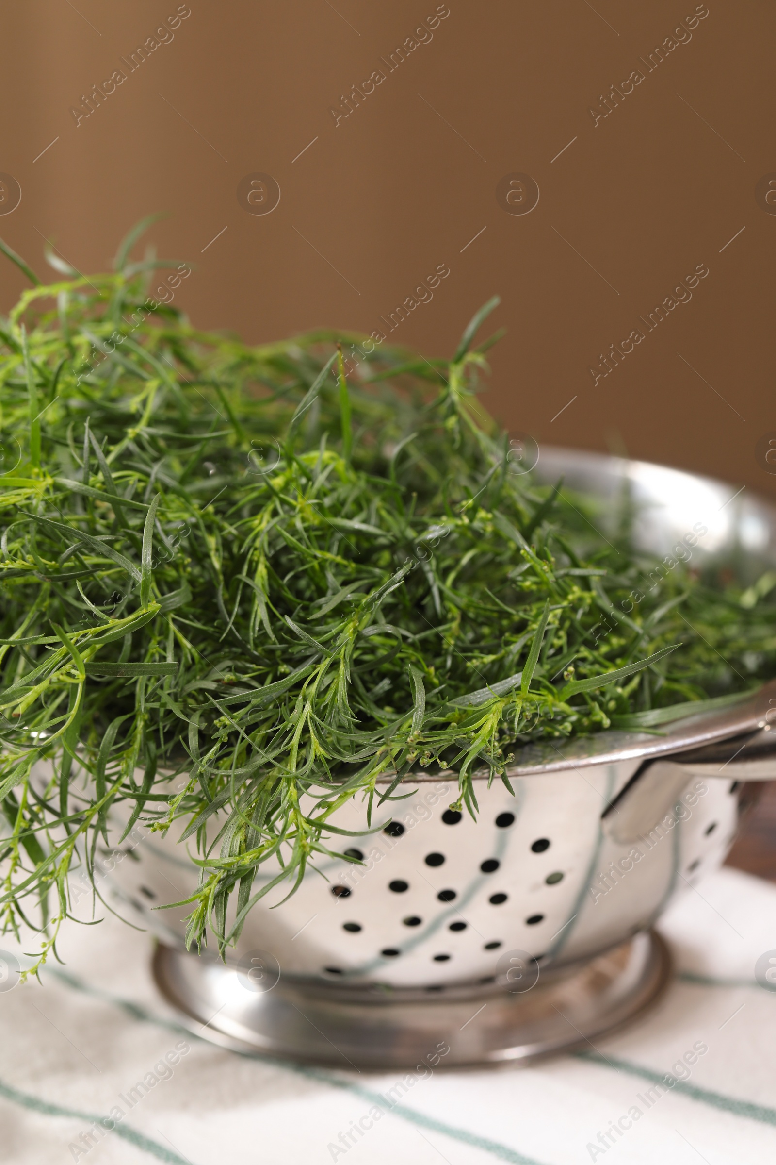 Photo of Colander with fresh tarragon leaves on table, closeup