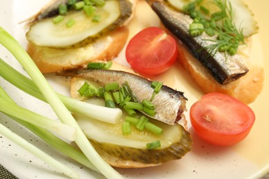 Photo of Delicious sandwiches with sprats, pickled cucumber and green onion served with tomato on plate, closeup