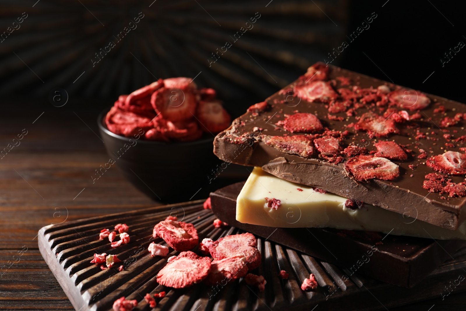 Photo of Board and different chocolate bars with freeze dried fruits on wooden table, closeup