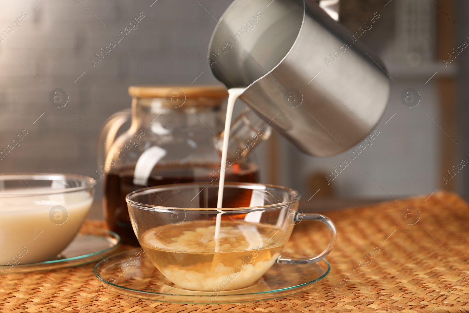 Photo of Pouring milk into glass cup at wicker mat, closeup