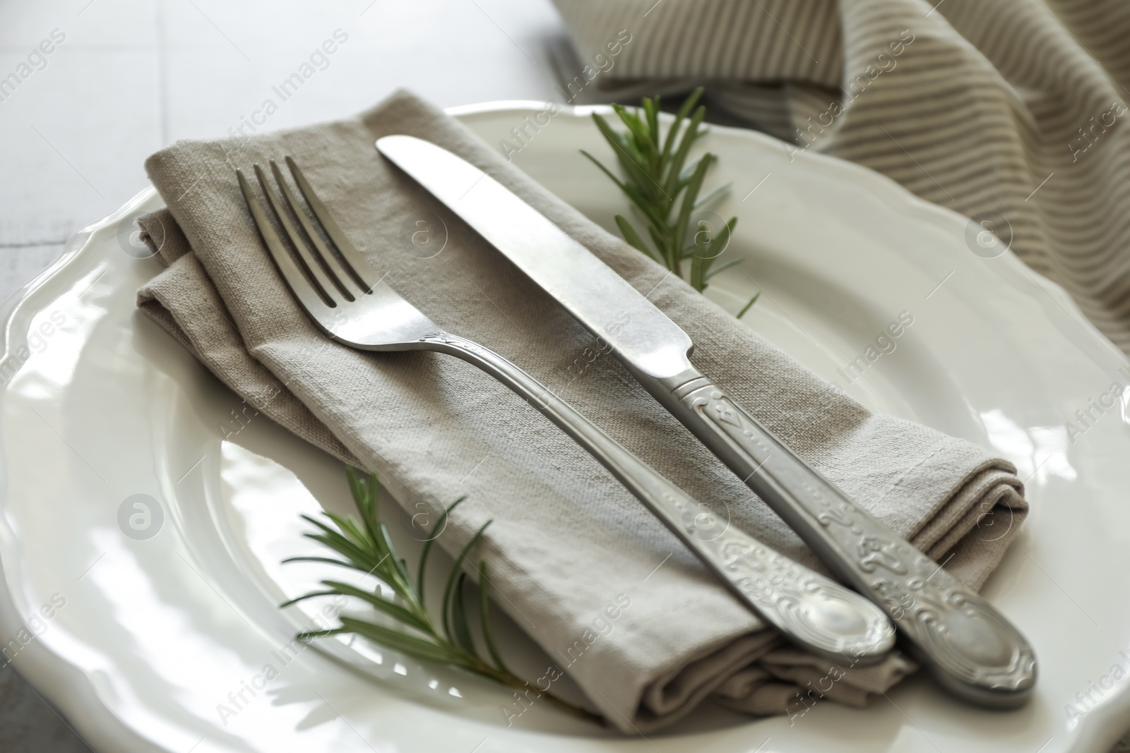 Photo of Stylish setting with cutlery, napkin, rosemary and plate on table, closeup