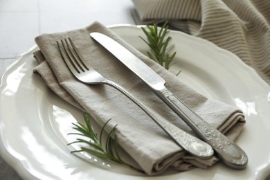 Stylish setting with cutlery, napkin, rosemary and plate on table, closeup