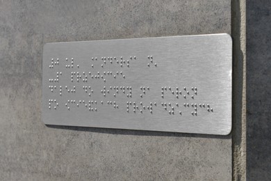 Photo of Silver plate with Braille text on grey wall, closeup
