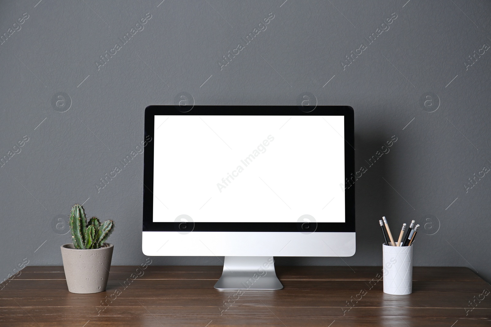 Photo of Modern computer monitor on table against gray wall. Mock up with space for text