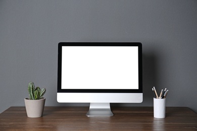 Photo of Modern computer monitor on table against gray wall. Mock up with space for text