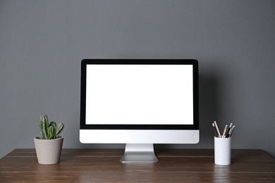 Modern computer monitor on table against gray wall. Mock up with space for text