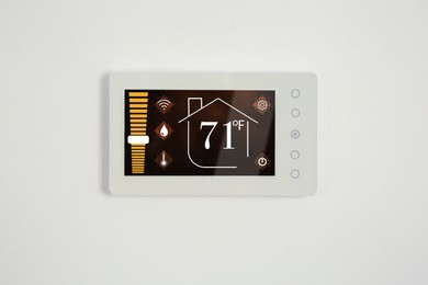 Image of Thermostat displaying temperature in Fahrenheit scale and different icons. Smart home device on white wall