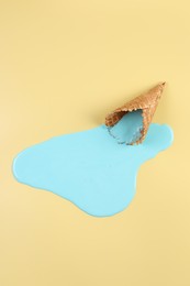 Melted ice cream and wafer cone on beige background, top view