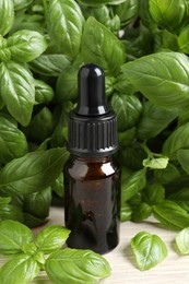 Photo of Glass bottle of basil essential oil and leaves on white wooden table