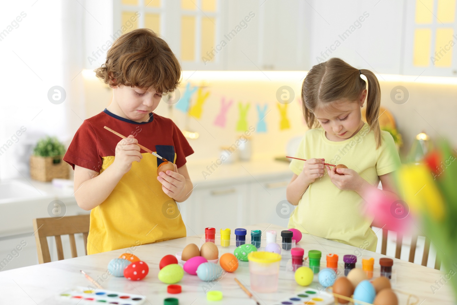 Photo of Easter celebration. Cute children painting eggs at white marble table in kitchen