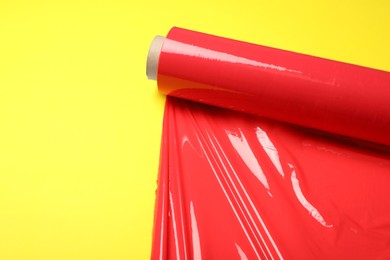 Photo of Roll of red plastic stretch wrap on yellow background. Space for text