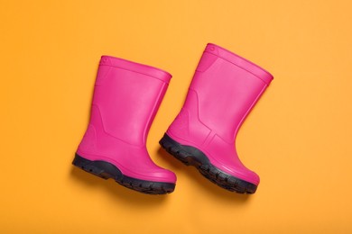 Photo of Pair of bright pink rubber boots on orange background, top view